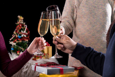 Midsection of friends toasting drinks during christmas celebration against black background