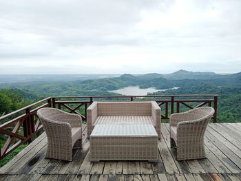 Empty chairs on railing against sky