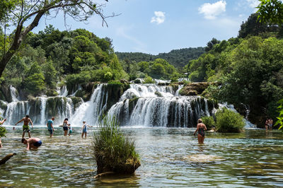 People at waterfall against sky