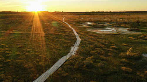 Road amidst field against sky during sunset