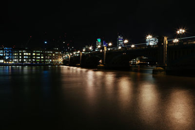 Illuminated bridge over river against sky at night