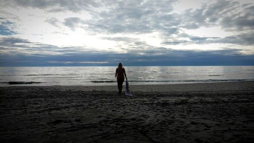 Rear view of woman standing on beach against sky