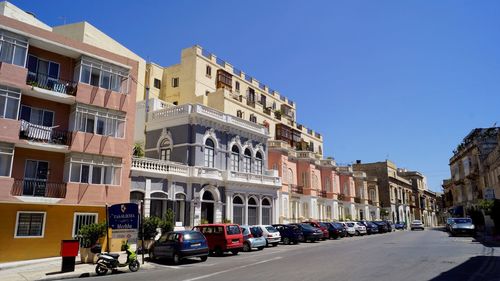 Road by cars and buildings against clear sky on sunny day