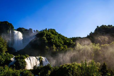 Scenic view of waterfall against clear blue sky