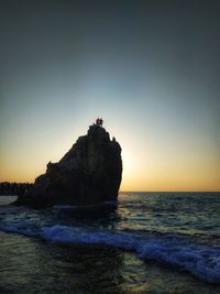 Rock formation on beach against sky during sunset