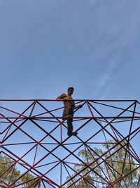 Low angle view of man standing on metallic built structure against clear blue sky