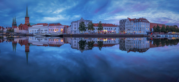 Church by buildings reflecting in lake during sunset