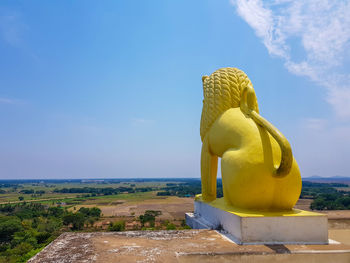 Sculpture of yellow statue against blue sky