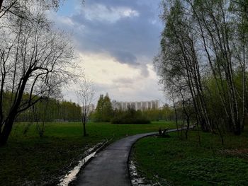Dirt road amidst trees on field against sky