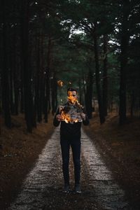Full length of man holding burning paper while standing on footpath amidst trees