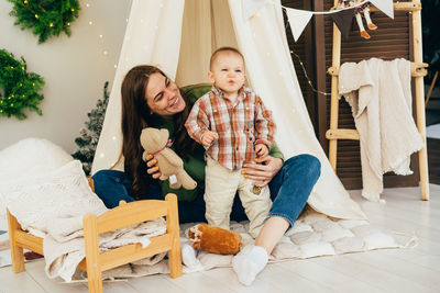 Young caring supportive mother playing with active emotional child in tent in the room.