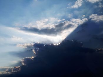 Low angle view of sunlight streaming through clouds