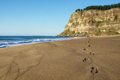 Footprints on beach by mountains against clear blue sky