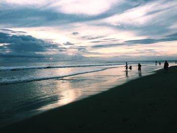 Silhouette people at beach against sky during sunset