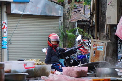 Side view of cute boy wearing helmet sitting on motorcycle against house