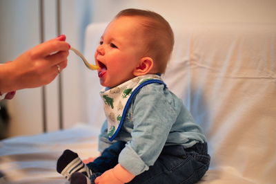 Midsection of mother feeding her baby son with spoon