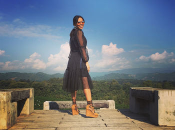 Young woman standing on rock against sky