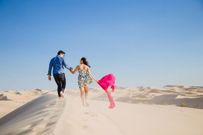 Rear view of couple walking on sand at desert against sky