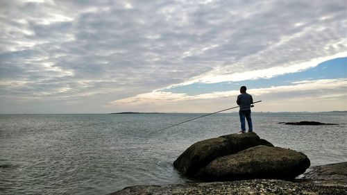 Man standing on rock by sea against sky