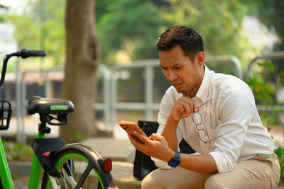 Side view of young man using mobile phone while sitting at park