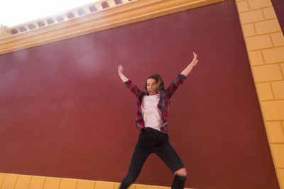 Cheerful woman jumping against maroon wall
