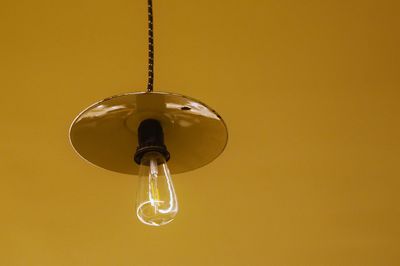 Close-up of light bulb hanging against yellow background