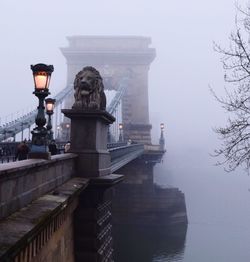 Low angle view of illuminated street light on chain bridge during foggy weather