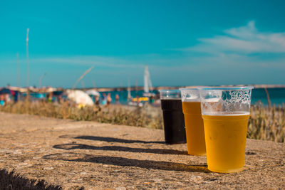 Close-up of glasses of beer on table against sky