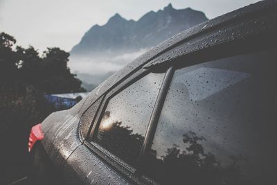 Close-up of wet car against sky during rainy season