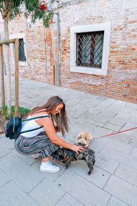 Side view of young woman with backpack petting dogs on footpath