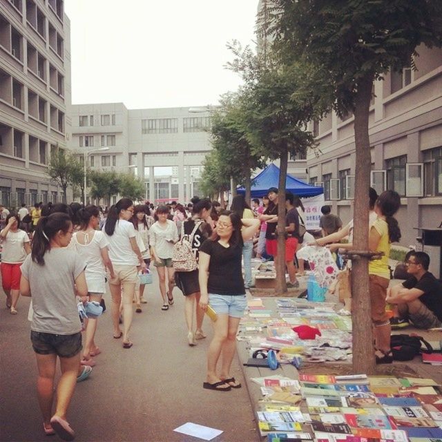 large group of people, men, person, building exterior, lifestyles, architecture, built structure, city, leisure activity, street, market, city life, crowd, walking, market stall, mixed age range, retail, casual clothing, street market