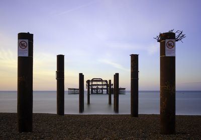 Information sign on wooden post at beach against sky