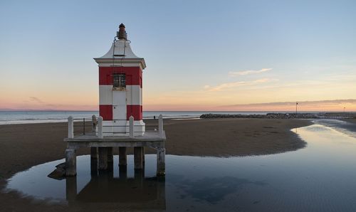 Lighthouse by sea against sky during sunset