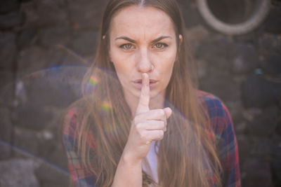 Portrait of woman with finger on lips against wall