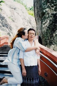 Woman kissing mother while standing on steps against rock formations