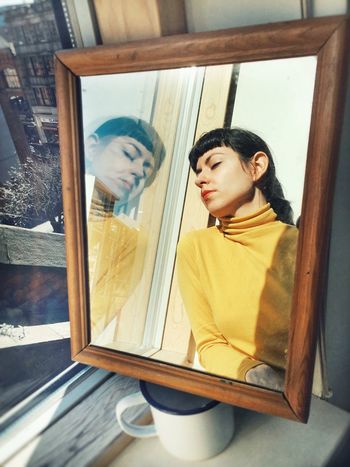 Young woman relaxing by glass window reflecting in mirror