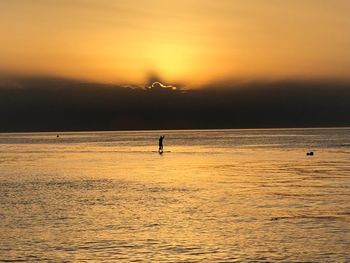 Silhouette person on sea against sky during sunset