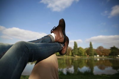 Low section of woman legs on man in park against sky