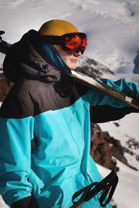 Young male skier in ski goggles stands with skis on his shoulder ready for competition. sportsman