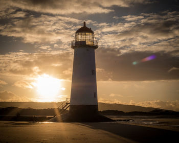 Lighthouse by sea against sky during sunset
