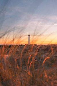 Lighthouse on field against sky during sunset