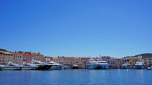 Boats moored in river in front of harbor against clear blue sky