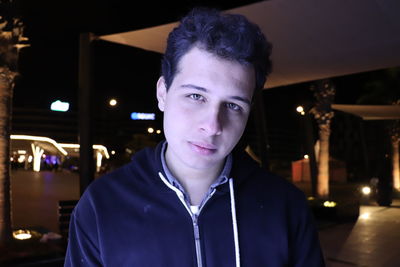 Portrait of young man standing against illuminated city at night