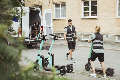 Male and female coworkers loading electric push scooter in delivery van