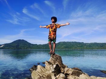 Full length of man standing on rock by lake against sky