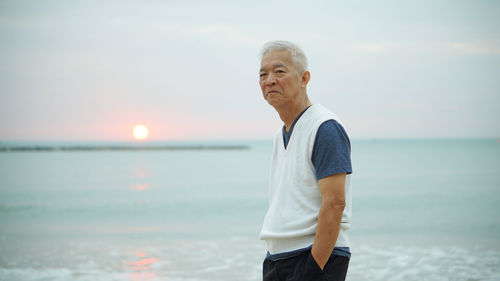 Portrait of man standing at beach against sky during sunset
