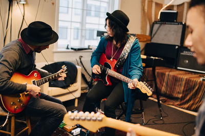 Male and female friends playing guitar while practicing at recording studio