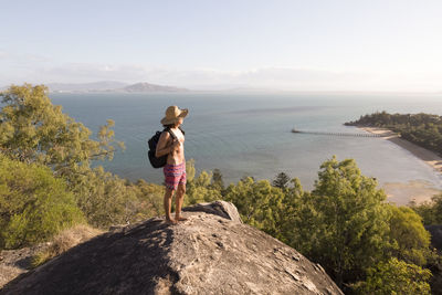 Backpacker with hat and swimsuit, on top of rocky hill during sunset