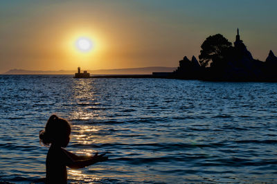 Silhouette person on sea against sky during sunset