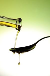 Cropped image of bottle pouring cooking oil on spoon against colored background